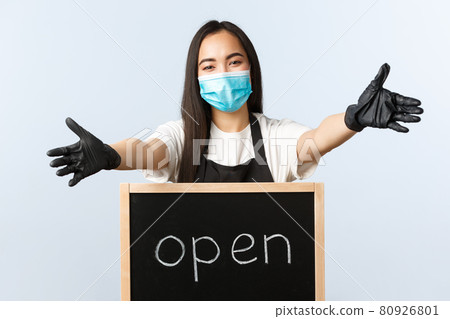 Small business, covid-19 pandemic, preventing virus and employees concept. Smiling friendly asian cafe worker, barista stretch hands in welcome or greeting, finally open for customers 80926801
