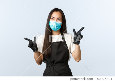 Covid-19, social distancing, small coffee shop business and preventing virus concept. Thoughtful asian barista, female cafe staff in medical mask and gloves pointing sideways, thinking making choice Covid-19, social distancing, small coffee shop business and preventing virus concept. Thoughtful asian barista, female cafe staff in medical mask and gloves pointing sideways, thinking making choice 80926804