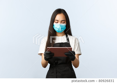 Covid-19, online orders, small coffee shop business and preventing virus concept. Young waitress in medical mask looking at digital tablet as taking order from cafe visitor, barista at work Covid-19, online orders, small coffee shop business and preventing virus concept. Young waitress in medical mask looking at digital tablet as taking order from cafe visitor, barista at work 80926831