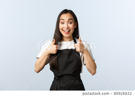 Coffee shop, small business and startup concept. Excited smiling asian waitress approve new menu. Cute female barista in black apron show thumbs-up in support, like or agree Coffee shop, small business and startup concept. Excited smiling asian waitress approve new menu. Cute female barista in black apron show thumbs-up in support, like or agree 80926832