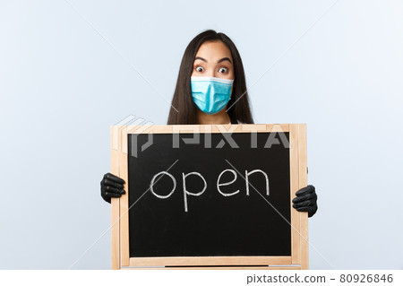 Small business, covid-19 pandemic, preventing virus and employees concept. Excited asian female cafe owner finally announce store open, wear medical mask, holding sign Small business, covid-19 pandemic, preventing virus and employees concept. Excited asian female cafe owner finally announce store open, wear medical mask, holding sign 80926846