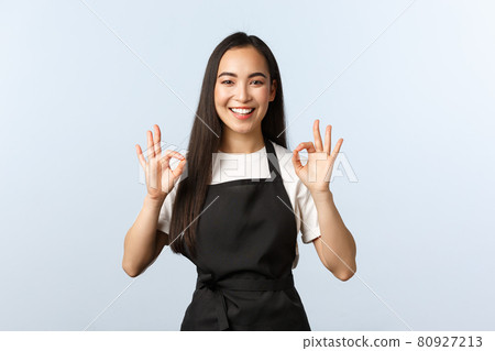Coffee shop, small business and startup concept. Smiling attractive korean female barista, waitress in cafe, black apron assure clients, show okay sign and grinning, no problem, guarantee quality Coffee shop, small business and startup concept. Smiling attractive korean female barista, waitress in cafe, black apron assure clients, show okay sign and grinning, no problem, guarantee quality 80927213