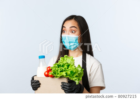 Covid-19, grocery store, employment, small business and preventing virus concept. Surprised asian female shop worker, cashier in medical mask and gloves raise eyebrows amused, hold bag with groceries Covid-19, grocery store, employment, small business and preventing virus concept. Surprised asian female shop worker, cashier in medical mask and gloves raise eyebrows amused, hold bag with groceries 80927215