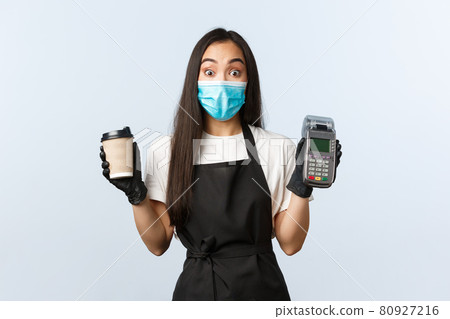 Coffee shop, coronavirus, social distancing and contactless payment concept. Surprised asian waitress, barista at cafe in medical mask and gloves with coffee order and POS terminal Coffee shop, coronavirus, social distancing and contactless payment concept. Surprised asian waitress, barista at cafe in medical mask and gloves with coffee order and POS terminal 80927216