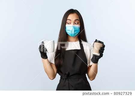 Covid-19, social distancing, small coffee shop business and preventing virus concept. Indecisive cute asian barista in medical mask decide what cup take, takeaway or regular Covid-19, social distancing, small coffee shop business and preventing virus concept. Indecisive cute asian barista in medical mask decide what cup take, takeaway or regular 80927329