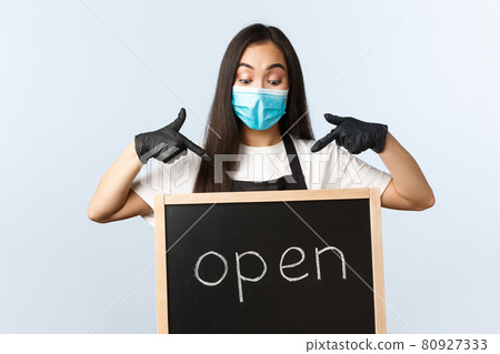 Small business, covid-19 pandemic, preventing virus and employees concept. Excited cute asian female barista, cafe or store worker in medical mask pointing at we are open sign Small business, covid-19 pandemic, preventing virus and employees concept. Excited cute asian female barista, cafe or store worker in medical mask pointing at we are open sign 80927333