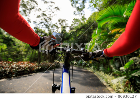 Cyclist using smart phone while riding bike on the spring forest trail Cyclist using smart phone while riding bike on the spring forest trail 80930127