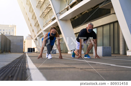 Fit middle aged couple on the start position, ready for running outdoors while wearing face protective masks during coronavirus outbreak Fit middle aged couple on the start position, ready for running outdoors while wearing face protective masks during coronavirus outbreak 80931458