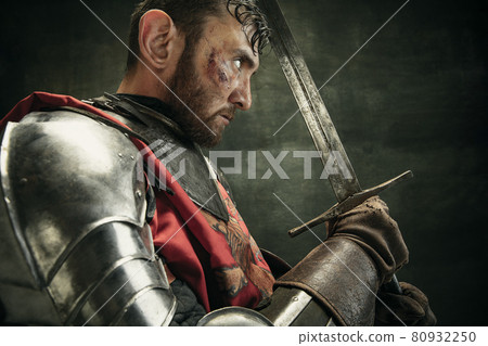 Side view. Portrait of one brutal bearded man, medeival warrior or knight with dirty wounded face holding sword 80932250