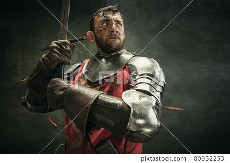 Portrait of one brutal bearded man, medeival warrior or knight with dirty wounded face holding sword 80932253