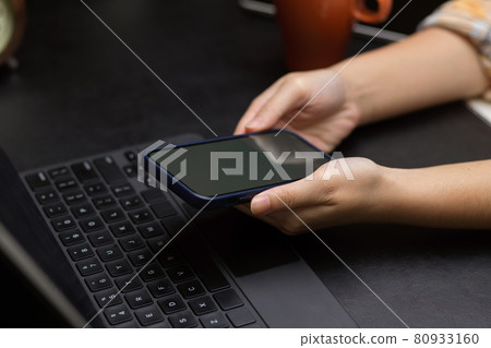female hands holding mobile phone with tablet keyboard on black working desk 80933160