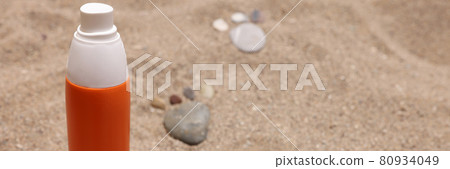 Orange jar of sunscreen standing on sand near stone footprints closeup Orange jar of sunscreen standing on sand near stone footprints closeup 80934049