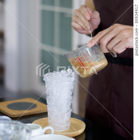 Clear plastic cup with ice for iced coffee on the table. Professional barista preparing coffee on counter. Clear plastic cup with ice for iced coffee on the table. Professional barista preparing coffee on counter. 80934917