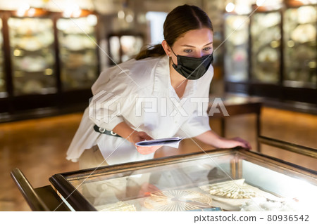 Woman in protective mask looking at exhibits in glazed stands in museum Woman in protective mask looking at exhibits in glazed stands in museum 80936542