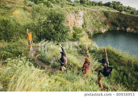 Beautiful landscape. Group of friends, young men and women walking, strolling together outskirts of city, in summer forest, meadow. Active lifestyle, friendship, care, ecology concept Beautiful landscape. Group of friends, young men and women walking, strolling together outskirts of city, in summer forest, meadow. Active lifestyle, friendship, care, ecology concept 80938953