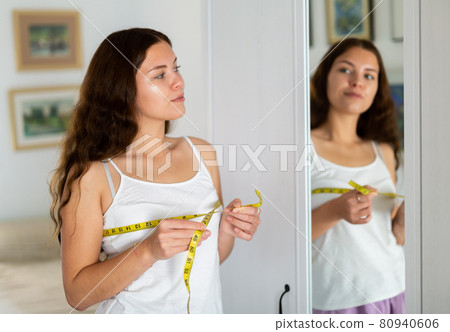 Happy young woman measuring breasts with measuring tape 80940606