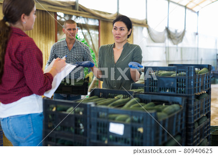 Two female managers are counting number of boxes of cucumbers, male worker carrying crates with cucumber Two female managers are counting number of boxes of cucumbers, male worker carrying crates with cucumber 80940625