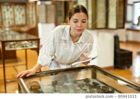 Woman looking at exhibits in glazed stands in museum 80941015