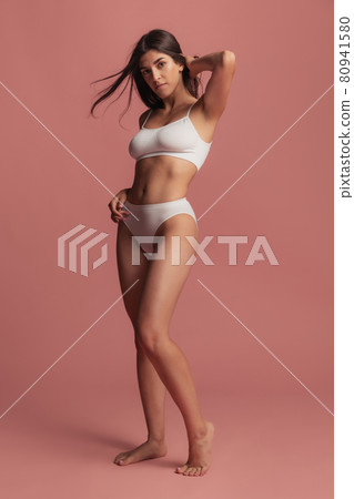 Portrait of young beautiful slim woman in lingerie posing isolated over pink studio background. Natural beauty concept. Portrait of young beautiful slim woman in lingerie posing isolated over pink studio background. Natural beauty concept. 80941580
