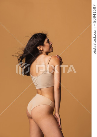 Back view of sportive body of young caucasian woman isolated on brown studio background. Natural beauty concept Back view of sportive body of young caucasian woman isolated on brown studio background. Natural beauty concept 80941597