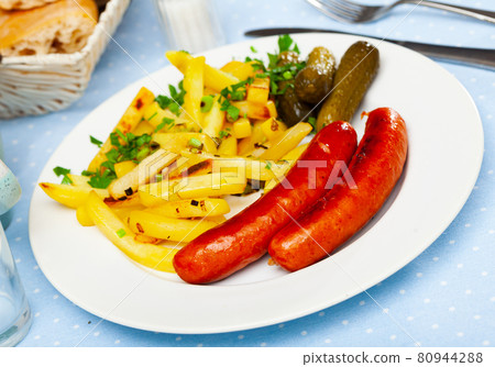 Appetizing sausages with potatoes and pickled cucumbers closeup Appetizing sausages with potatoes and pickled cucumbers closeup 80944288