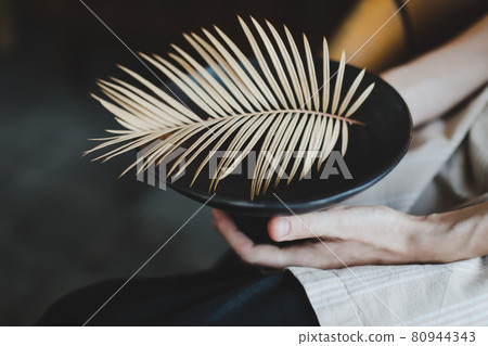 female hands holding a black ceramic plate decorated with fern leaf close-up female hands holding a black ceramic plate decorated with fern leaf close-up 80944343
