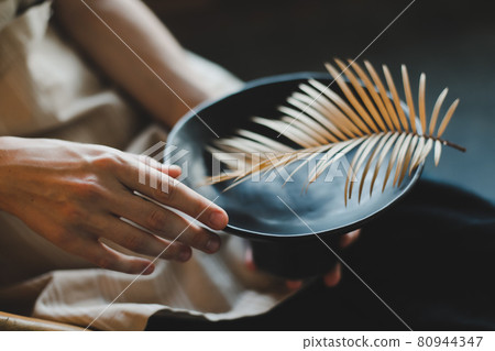 female hands holding a black ceramic plate decorated with fern leaf close-up 80944347