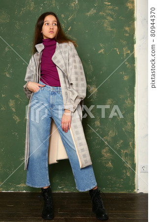 woman in checkered trench coat, jeans and bootswalking full body portrait on green wall background woman in checkered trench coat, jeans and bootswalking full body portrait on green wall background 80944370