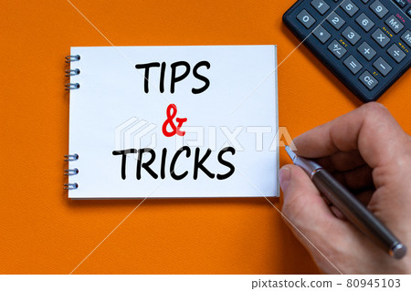Tips and tricks symbol. Businessman writing words 'Tips and tricks' on white note. Black calculator. Beautiful orange background. Business, tips and tricks concept. Copy space. Tips and tricks symbol. Businessman writing words 'Tips and tricks' on white note. Black calculator. Beautiful orange background. Business, tips and tricks concept. Copy space. 80945103