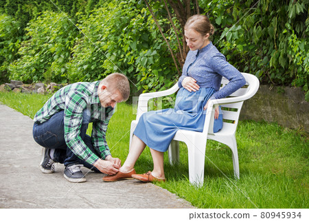 Husband ties the laces on the shoes of his pregnant wife 80945934