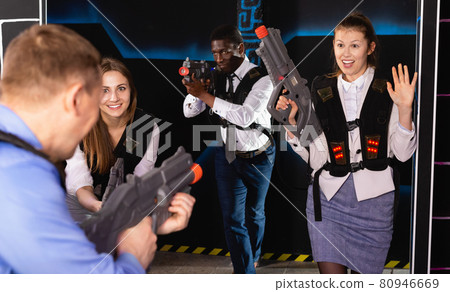 Men and women in business suits playing laser tag emotionally in dark room 80946669