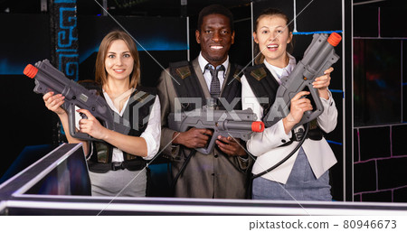 Smiling associates - afro man and two European women posing at laser tag room Smiling associates - afro man and two European women posing at laser tag room 80946673