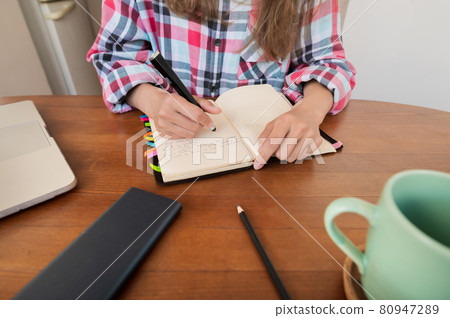 Young woman sitting at the kitchen table makes notes in a notebook. Home Office. Caucasian girl being homeschooled 80947289