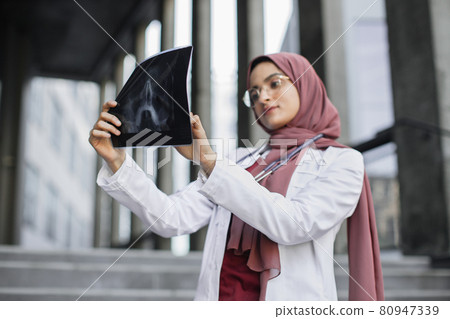 Muslim woman surgeon, looking at X-Ray radiography of patient's head skull Muslim woman surgeon, looking at X-Ray radiography of patient's head skull 80947339