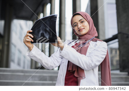 Close waist up portrait of smiling Muslim woman doctor holding an x-ray. Close waist up portrait of smiling Muslim woman doctor holding an x-ray. 80947342