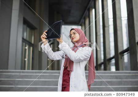 Malay lady doctor radiologist, looking at Xray results, standing outdoors Malay lady doctor radiologist, looking at Xray results, standing outdoors 80947349