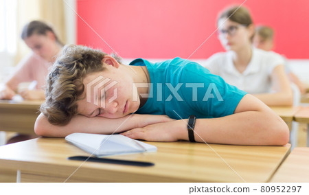 Bored teenage boy sleeping at desk in classroom during lesson 80952297