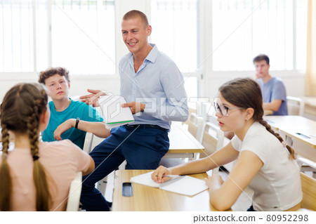 Friendly teacher discussing with teen students in classroom 80952298