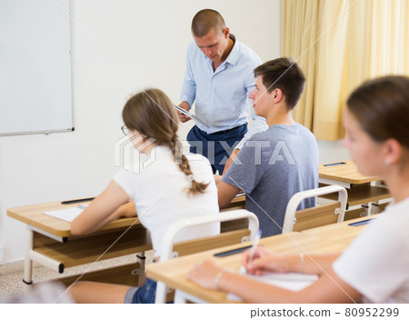 Teenage students are sitting at their desks in classroom. In background the teacher 80952299
