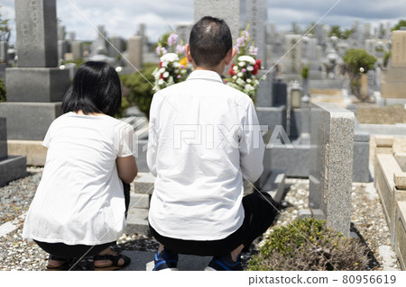 Middle-aged couple visiting a grave and holding hands 80956619