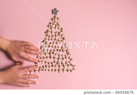 Female hands decorating golden Christmas tree on pink background. View from above. Flat lay Female hands decorating golden Christmas tree on pink background. View from above. Flat lay 80956676