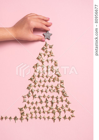 Female hands decorating golden Christmas tree made of beads on pink background. View from above. Flat lay 80956677