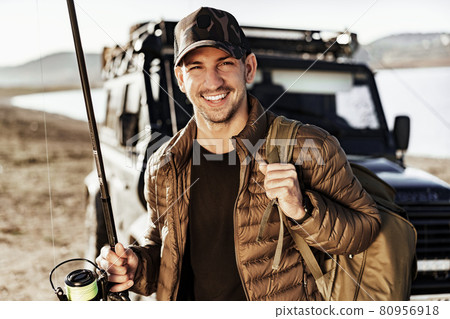 Young fisherman standing near his car and holding fishing equipment 80956918