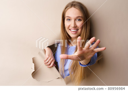 Beautiful young woman looking through a hole in beige paper 80956984