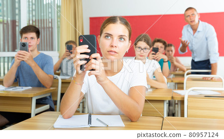 Girl high school student using mobile phone on lecture in class Girl high school student using mobile phone on lecture in class 80957124