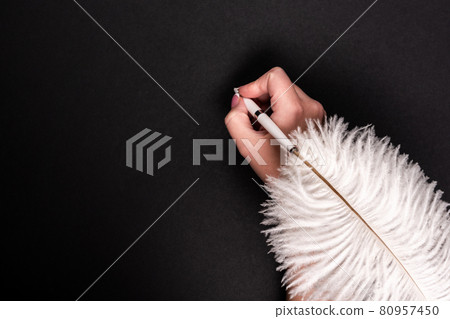 Female hand holding feather pen over black surface 80957450