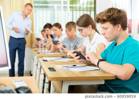 Teenager student using mobile phone at lesson in classroom Teenager student using mobile phone at lesson in classroom 80959059