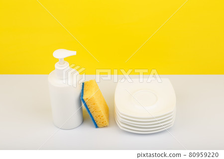 Dishwashing detergent in white bottle, pile of saucers and cleaning sponge against yellow background Dishwashing detergent in white bottle, pile of saucers and cleaning sponge against yellow background 80959220