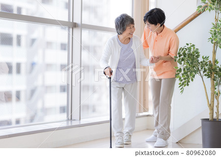 Care image: Senior woman walking with a cane and a caregiver 80962080