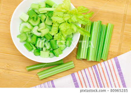 Fresh Chopped Celery Slices in White Bowl with Celery Sticks on Bamboo Cutting Board Fresh Chopped Celery Slices in White Bowl with Celery Sticks on Bamboo Cutting Board 80965285
